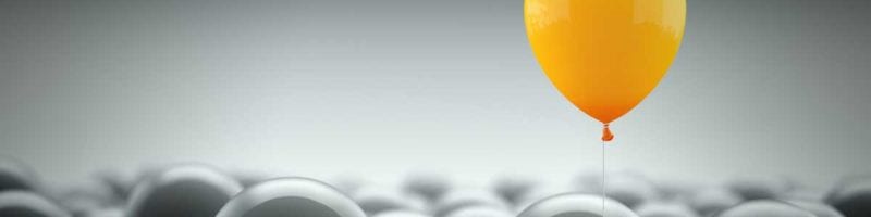 Yellow balloon rising above grey balloons