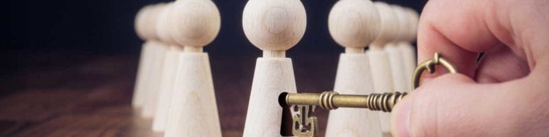 someone putting a key into lock on small wooden representation of a person